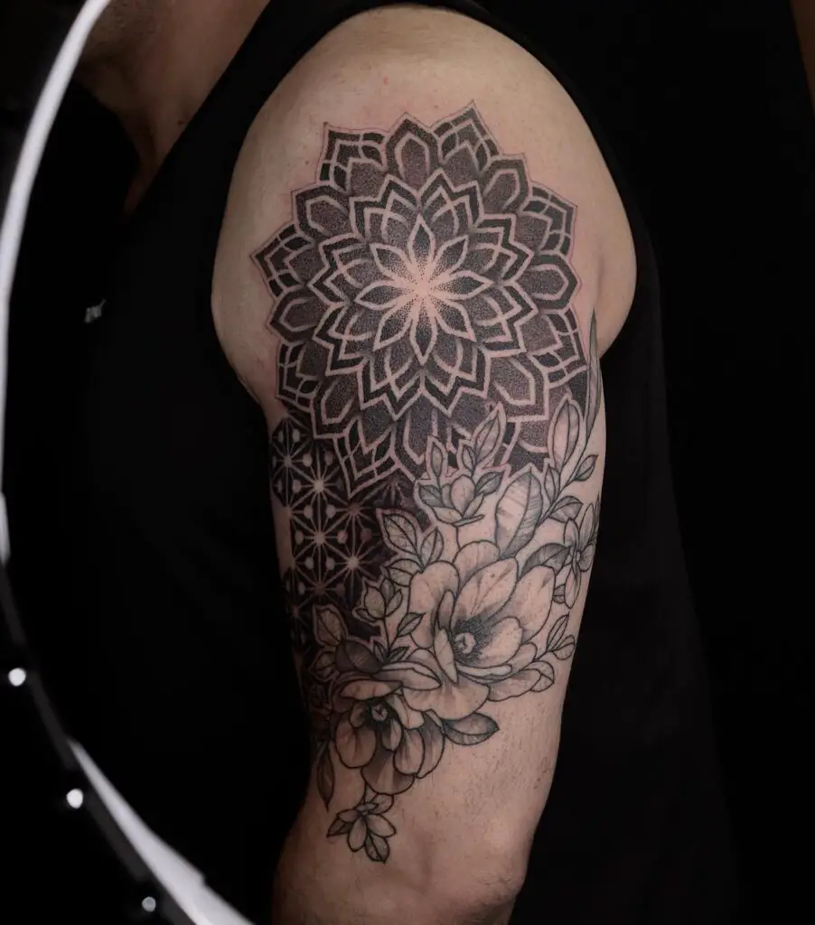 A sleeve tattoo with a central mandala pattern extending into realistic magnolia flowers.