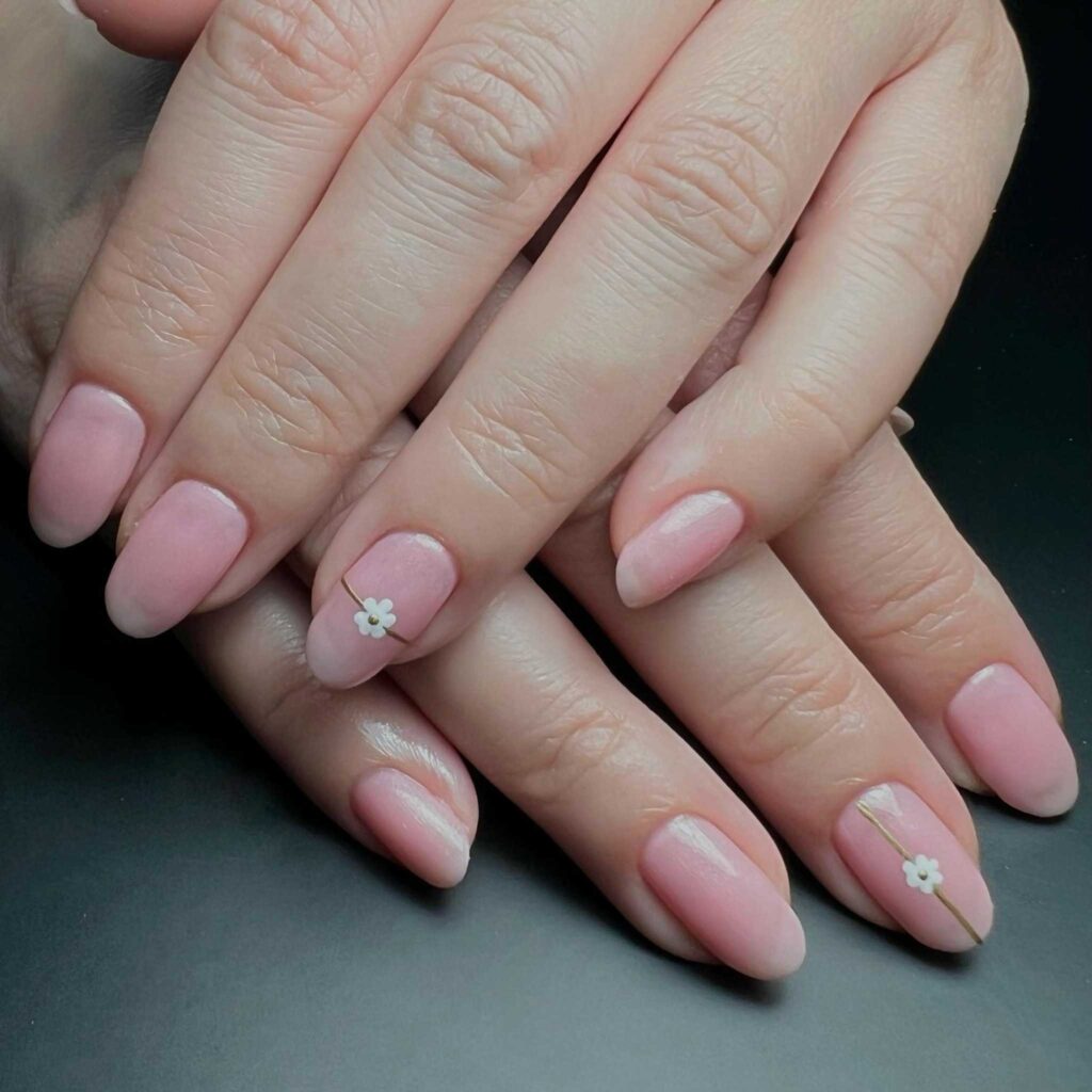 Hand with matte pink nails, each featuring a delicate white flower, embodying simplicity and elegance.