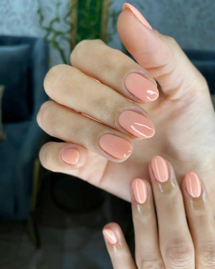 Hand with nails painted in a calming soft peach hue, providing a natural, understated look.