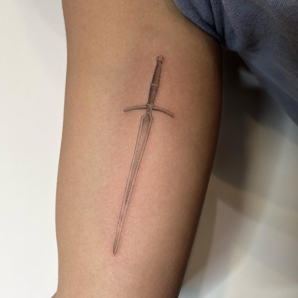 A simple, vertical sword tattoo on the arm, embodying elegance and strength.