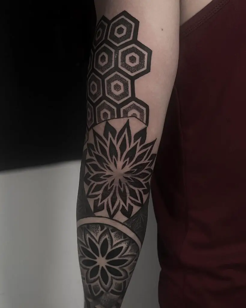 An arm tattoo with an interlocking hexagon pattern transitioning into a floral mandala, resembling an arm band.