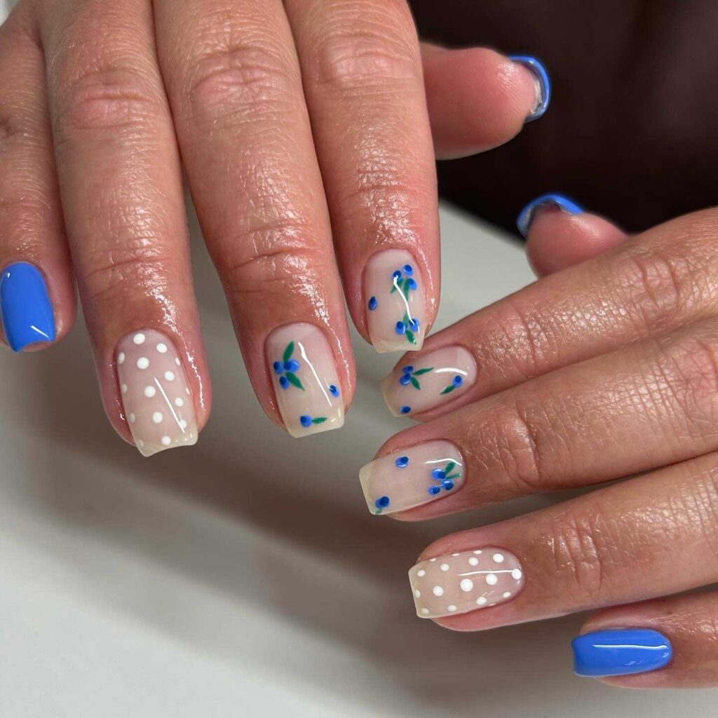 A lively combination of blue floral nail art and white polka dots on neutral-colored nails, radiating a cheerful retro flair.