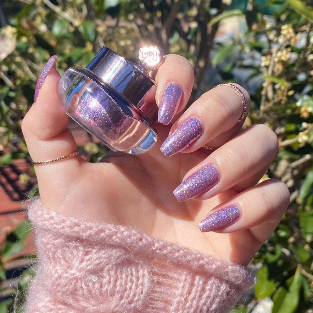 Fingers with lavender sparkling nail polish holding a polish bottle, with a springtime vibe in the bright, natural light.