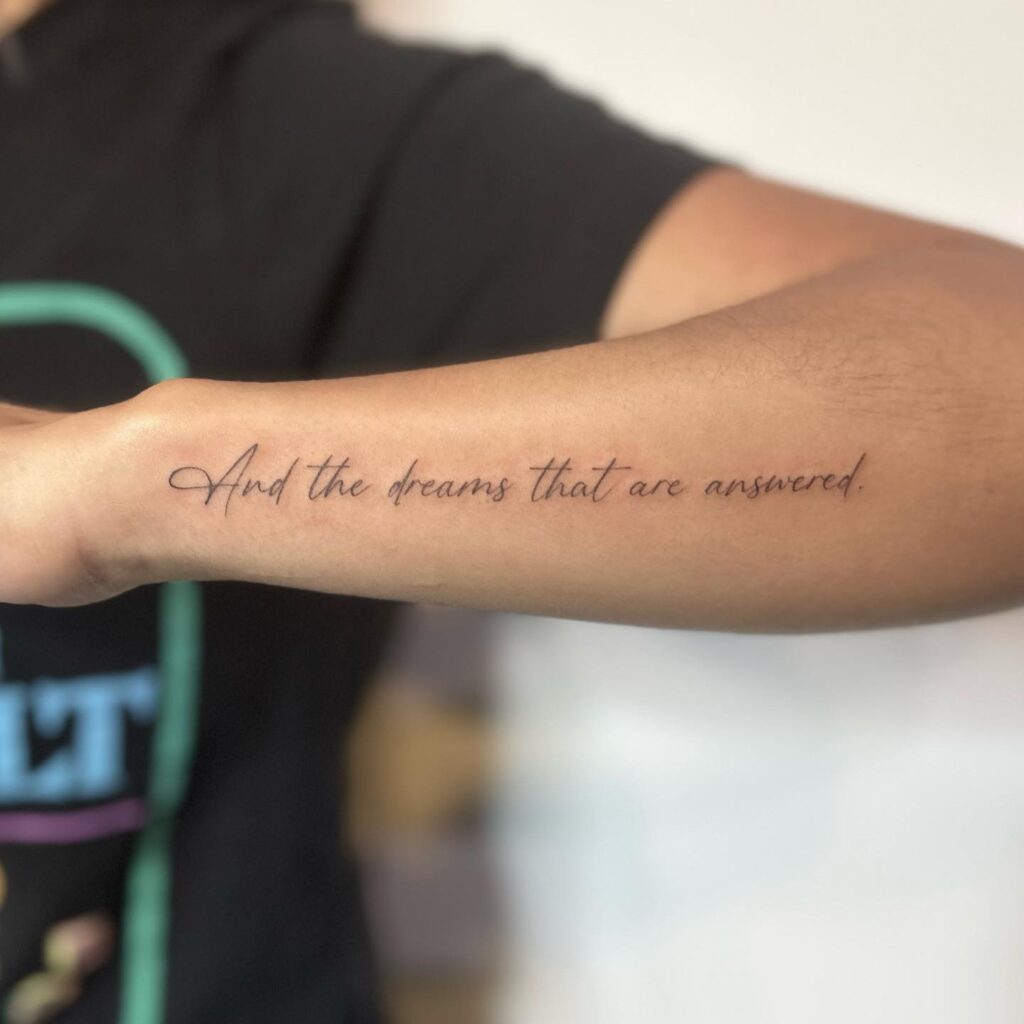 A forearm tattoo with the script "And the dreams that are answered," celebrating fulfillment and literature.