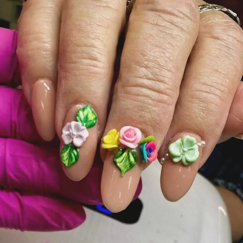 Nails featuring colorful 3D floral appliques and green leaves on a neutral nail base, expressing a bold and textured look.