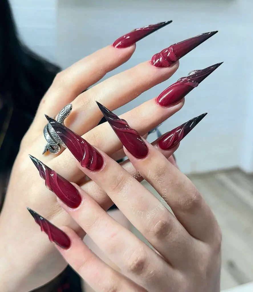 Sharp, pointed nails in a glossy maroon shade, evoking a sense of gothic glamour and bold style.