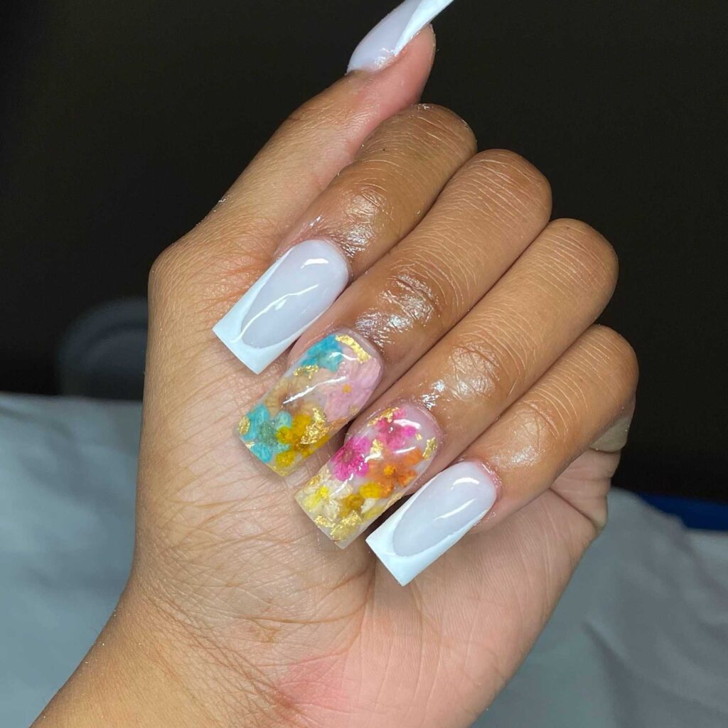 A mix of clear and white-tipped nails with gold foil and colorful abstract floral patterns, showcasing a unique artistic flair.