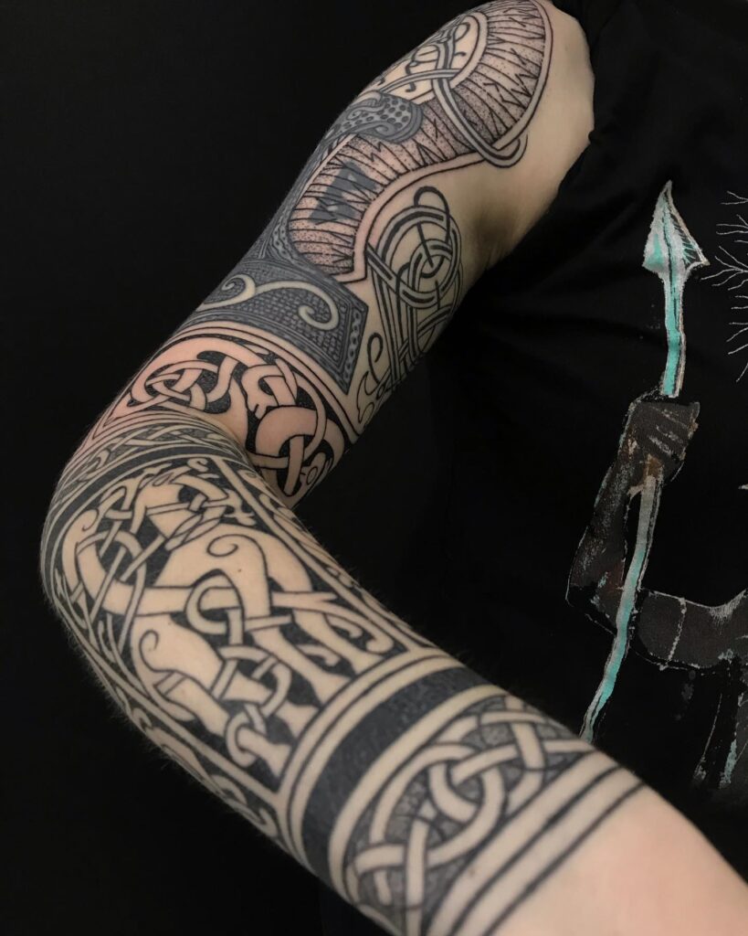 A detailed forearm tattoo featuring the Helm of Awe symbol with Norse knotwork in black and gray shading.