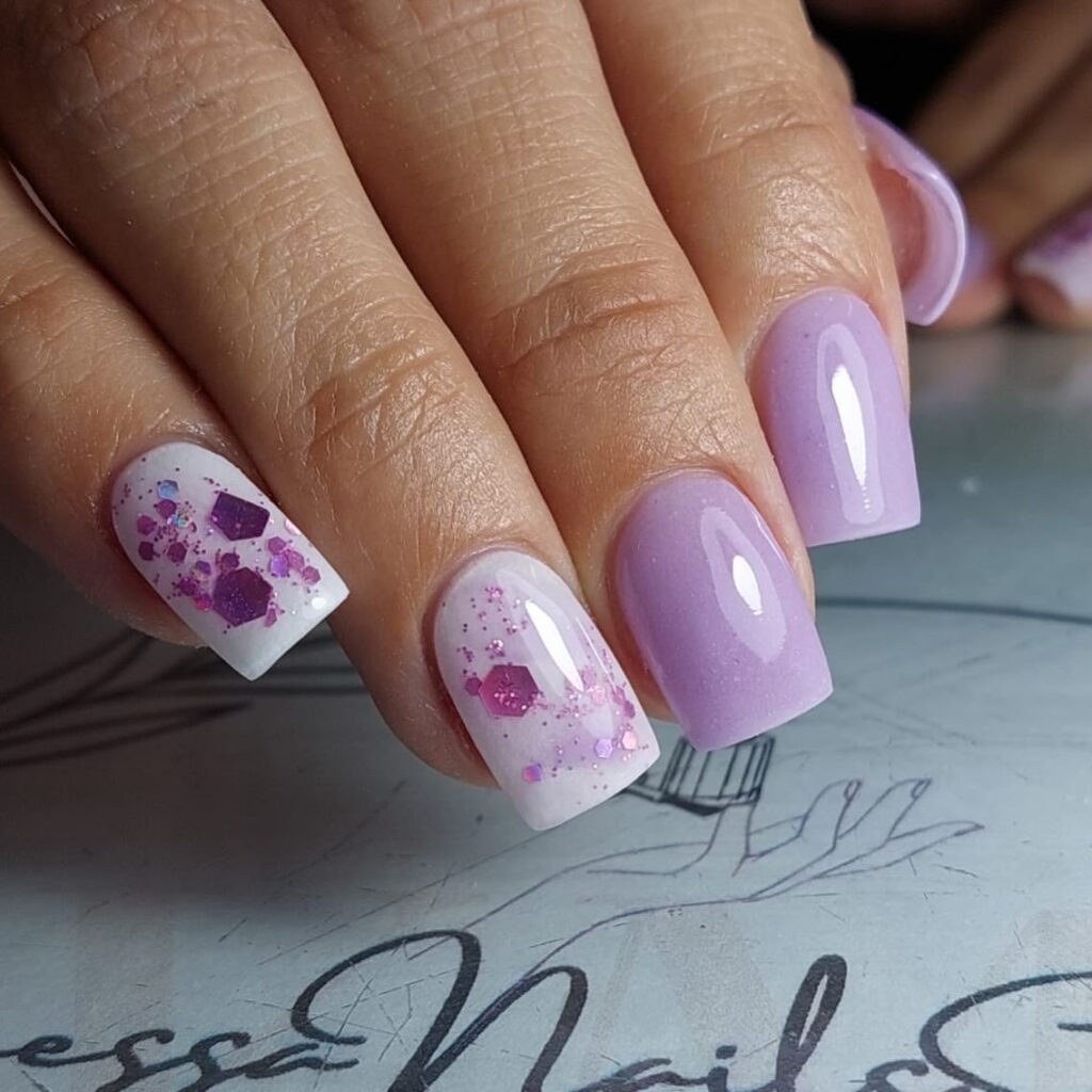 Close-up of nails painted in a pastel lilac color with white and pink glitter accents, evoking the freshness of spring flowers.