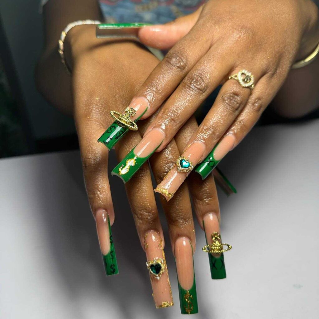 Long nails with emerald green tips, gold foil accents, and decorative jewelry, exuding opulence and luxury.