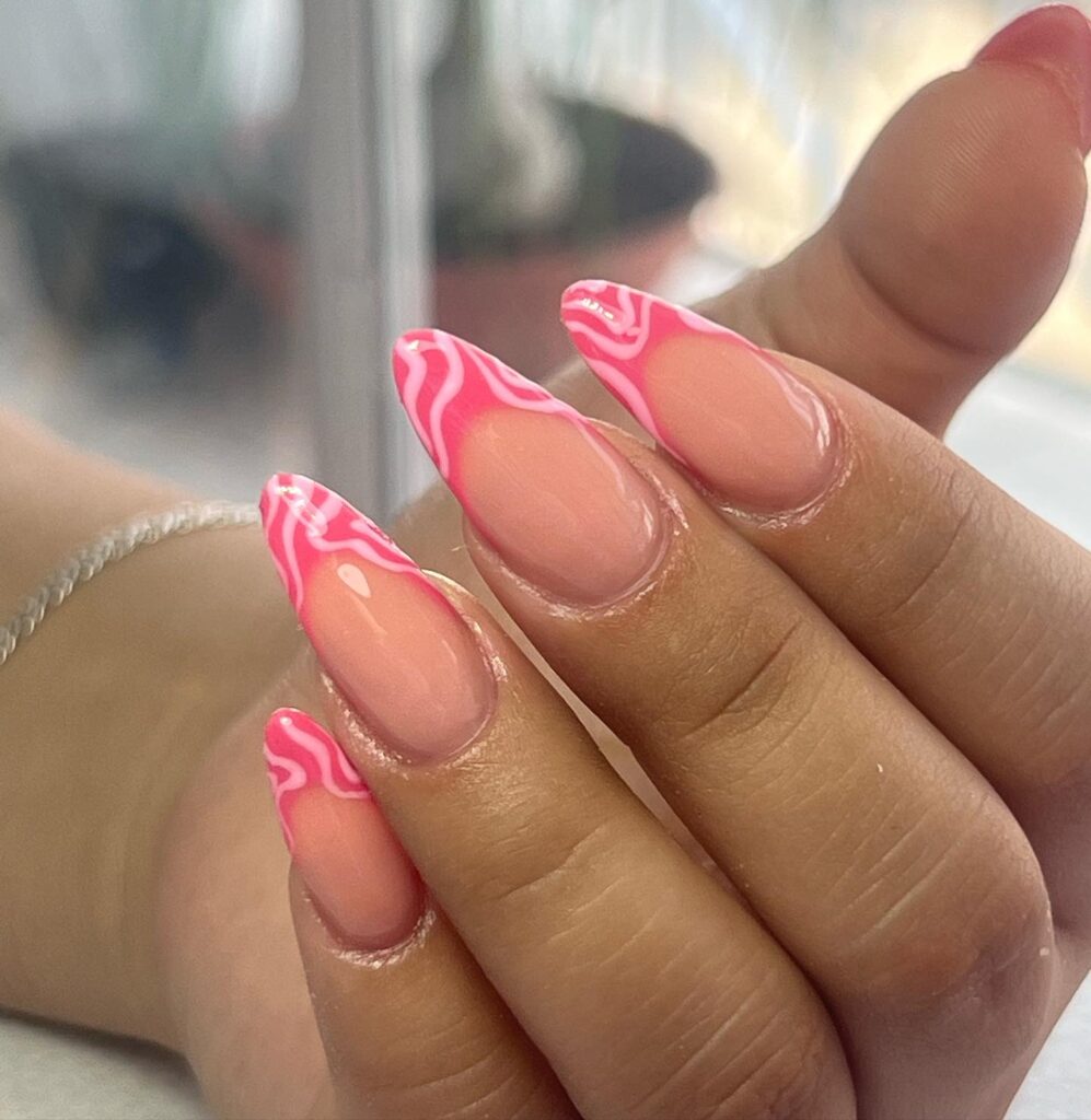 Close-up of a hand with nails painted in a sheer pink base and detailed with vibrant hot pink flame patterns for a sizzling look.