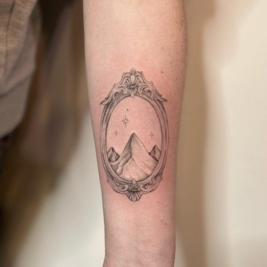 A leg tattoo of mountains within a vintage mirror frame, reflecting timeless elegance and the majesty of nature.